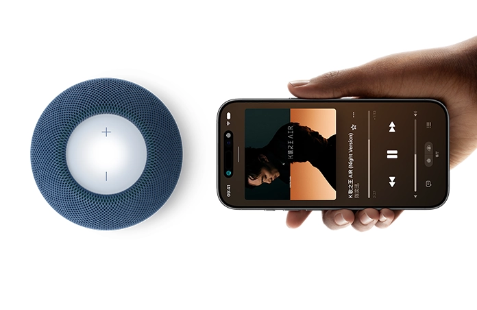HomePod mini 2 和 iPhone：一只手将 iPhone 放在蓝色 HomePod mini 2 旁边，以启用接力功能。
