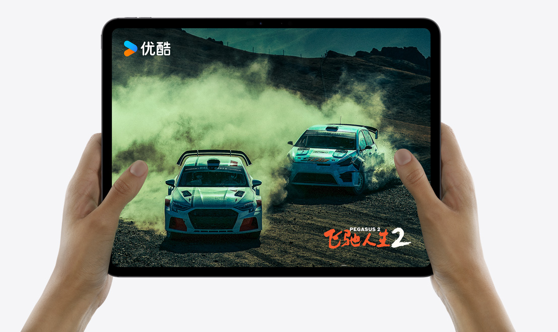 一双手拿着 iPad Pro，屏幕上显示优酷 app 上的《飞驰人生 2》