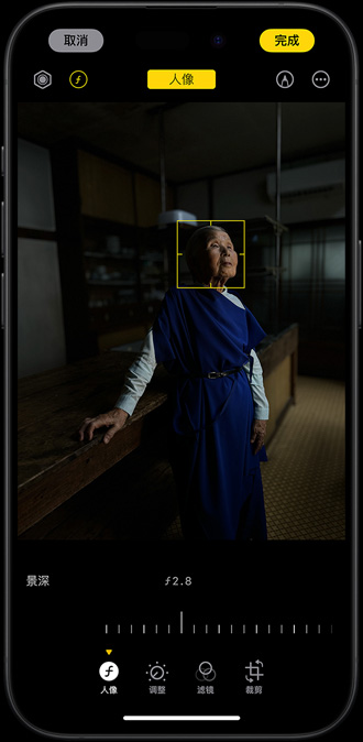 低光环境下，一部 iPhone 15 Pro 正在为一位妇人拍摄人像，可调节的焦点聚焦在她的脸部