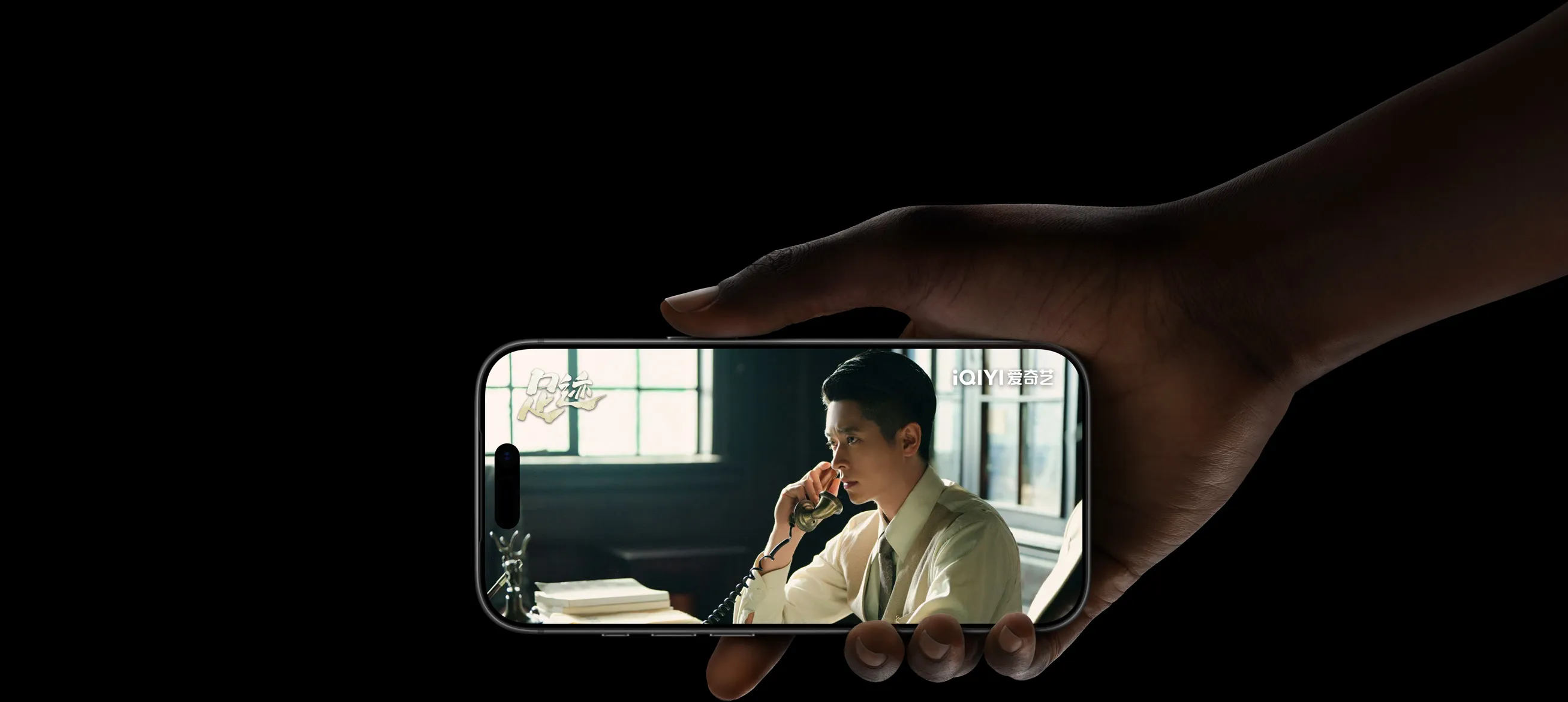 一只手拿着横屏的 iPhone 17 Pro，屏幕显示爱奇艺 app 正在播放剧集《足迹》的画面，体现 iPhone 17 Pro 电池续航进一步提升。