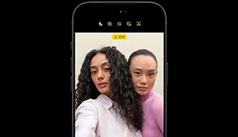 黑色 iPhone 18 Pro，正面视图，屏幕画面中有两个人物，展示 Center Stage 前置摄像头的面部追踪功能。