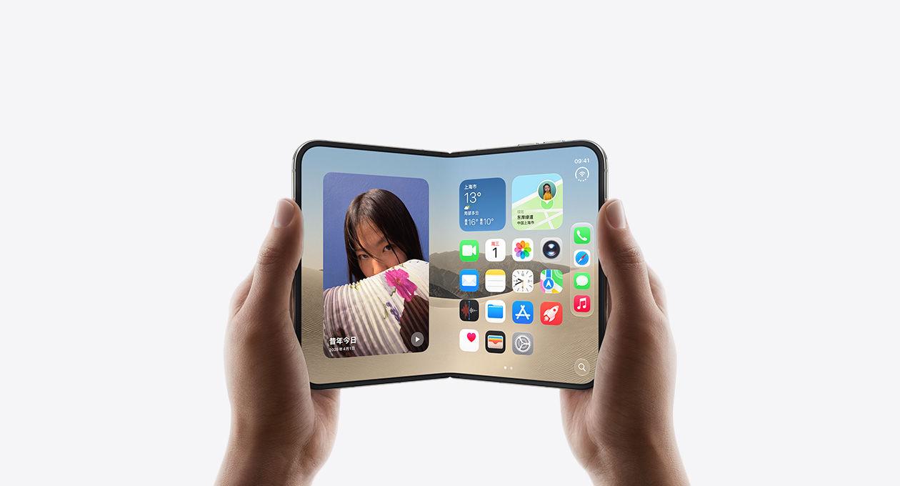 两只手拿着一部展开的星光白色 iPhone Duo，横屏姿态展示内屏，显示 iOS 主屏幕，屏幕左边是照片，右边是各种 app。