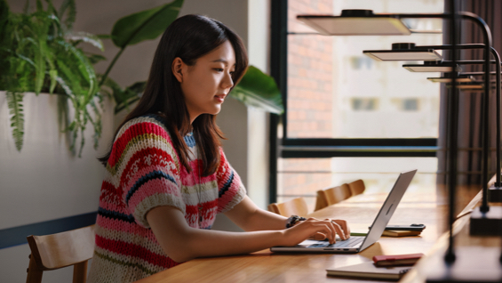 照片展示大学图书馆里，一位女生正坐在书桌前使用 MacBook Pro。
