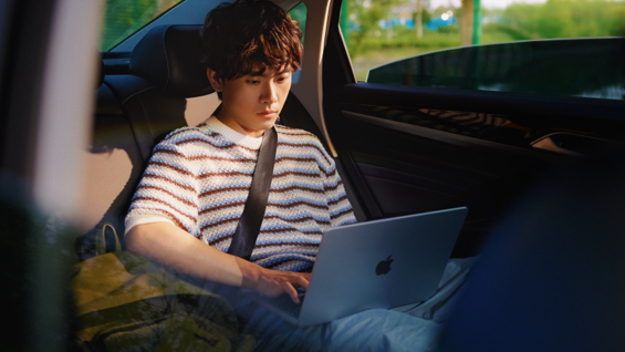 照片展示一个男生坐在轿车后排用着 MacBook Air。