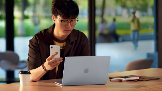 照片展示一位男生在室内，同时使用 MacBook Air 和 iPhone Air。