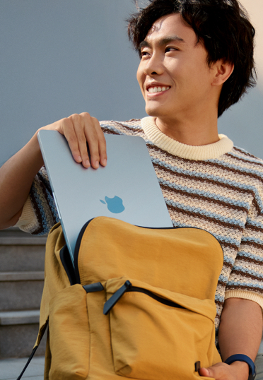 一名学生在户外。他从书包里拿出一台合上的 MacBook Air。