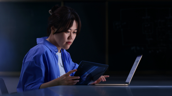 照片展示一位女生坐在书桌前用着 MacBook Air，同时一手拿着一张 X 光片。