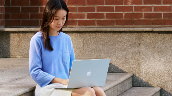 照片展示一位学生在户外正在使用 Macbook Air。