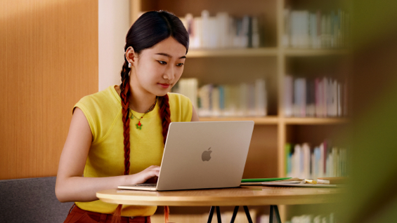 照片展示大学图书馆里，一位女生正坐在书桌前用着 MacBook Air。