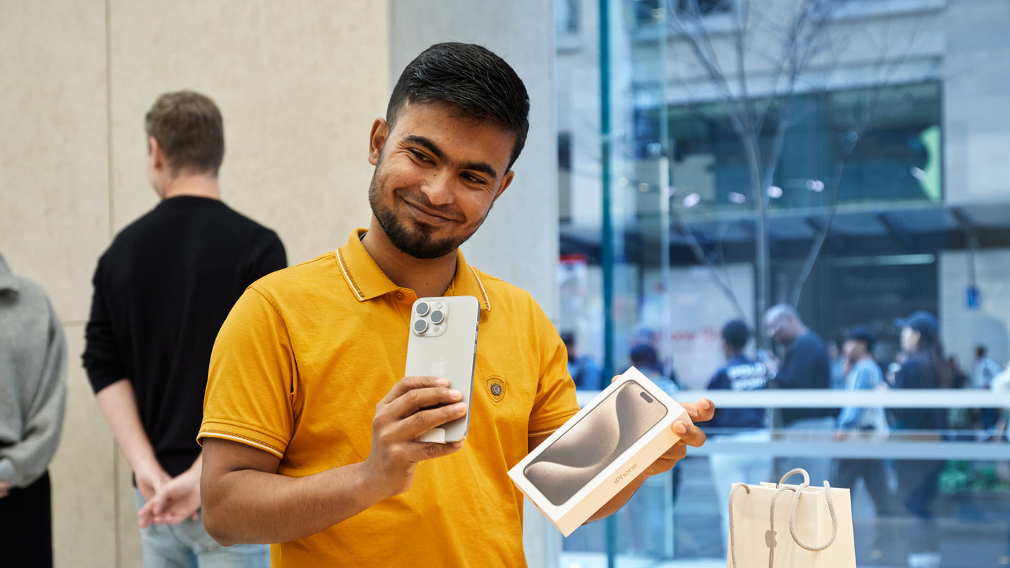 澳大利亚 Apple 悉尼零售店内，一位开心的顾客手持全新 iPhone 15 Pro。