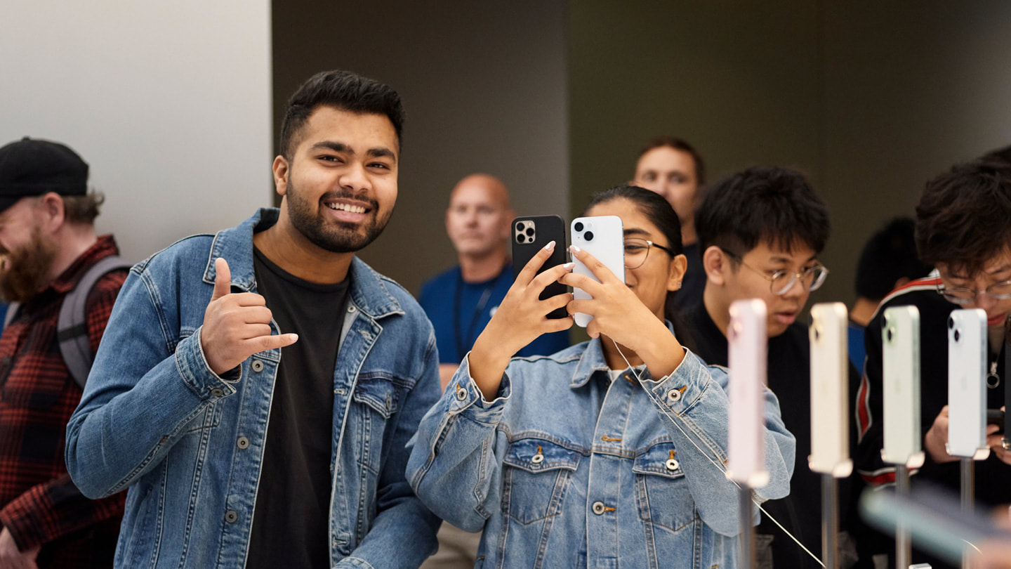 澳大利亚 Apple 悉尼零售店内，两位顾客面带笑容，手持 iPhone 设备。