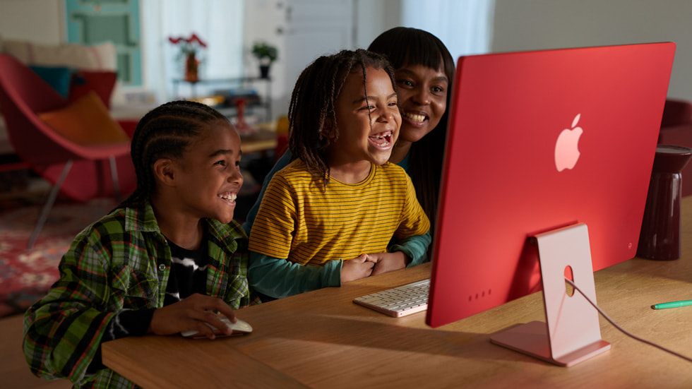 图中是两名儿童和一名家长，正在使用搭载 M3 芯片的粉色新款 iMac 以及同系列配色的键盘和鼠标。