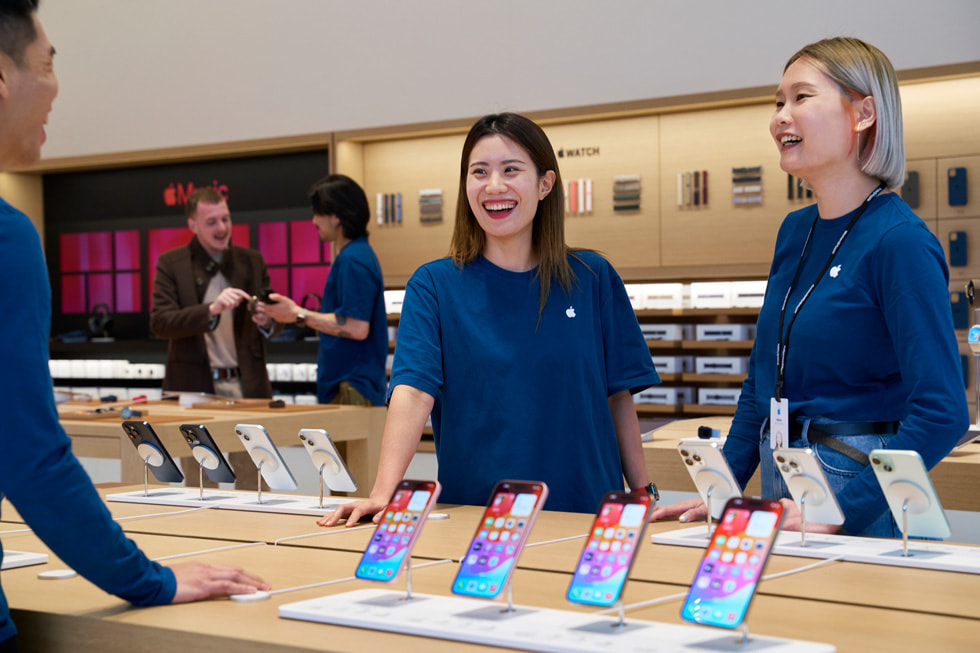 三名团队成员站在最新 iPhone 系列产品的展示桌旁。