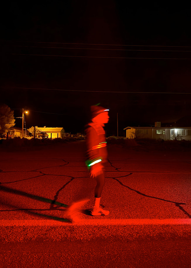 一位跑者在夜间佩戴着反光装备在公路上奔跑。