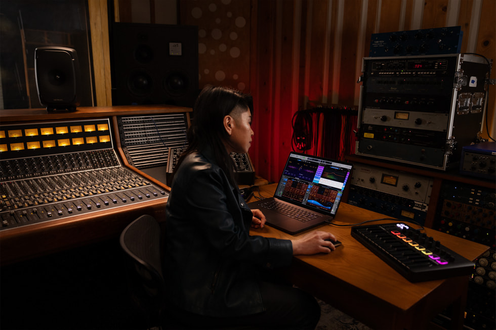 图片展示一位 Logic Pro 用户在音乐工作室内使用 MacBook Pro 工作。