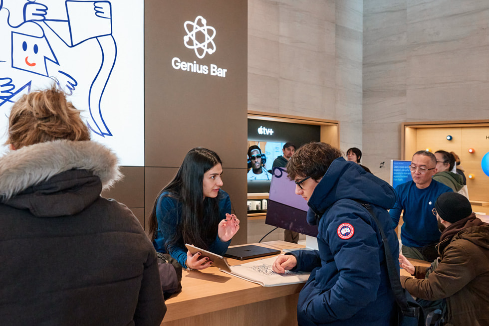 Apple Sainte-Catherine 零售店内，一位顾客在 Genius Bar 天才吧与 Specialist 专家交谈。