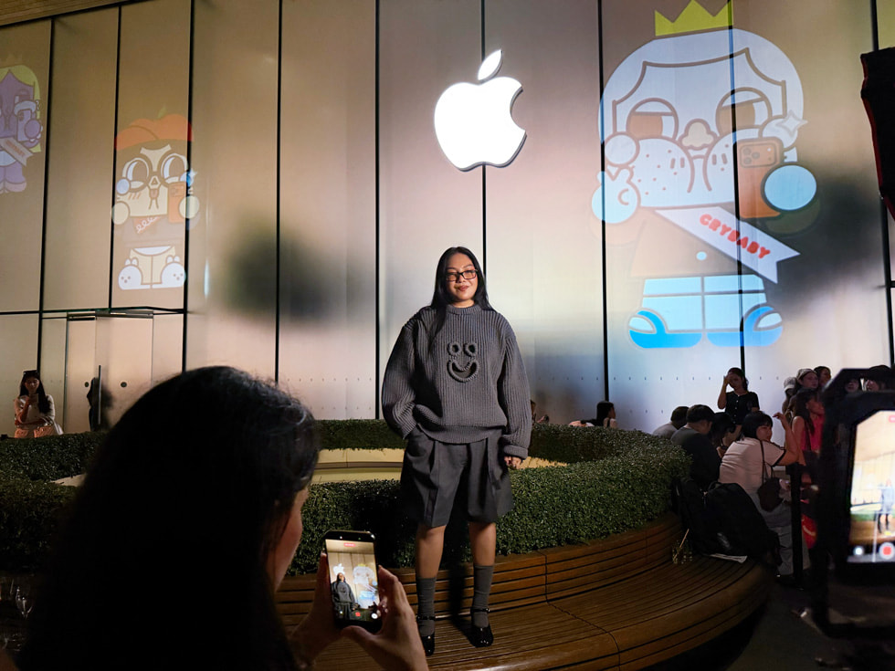 曼谷 Apple Iconsiam 零售店内，画家 Molly Yllom 面对 iPhone 摆出姿势拍照。