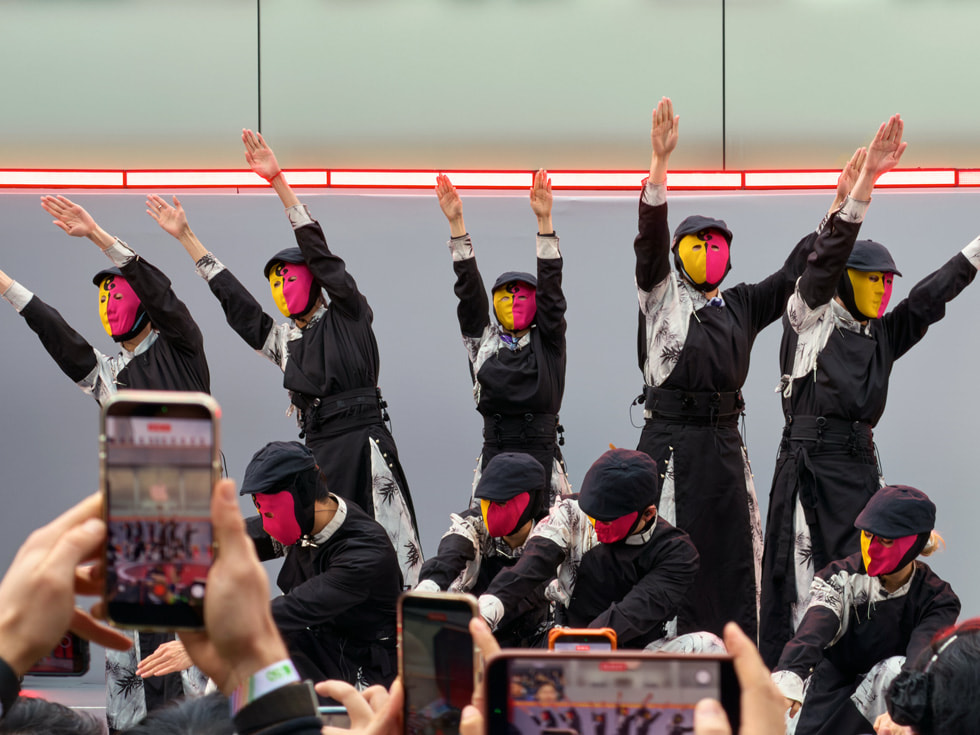 头戴橙红两色脸谱的舞者在中国 Apple 成都太古里零售店外表演。