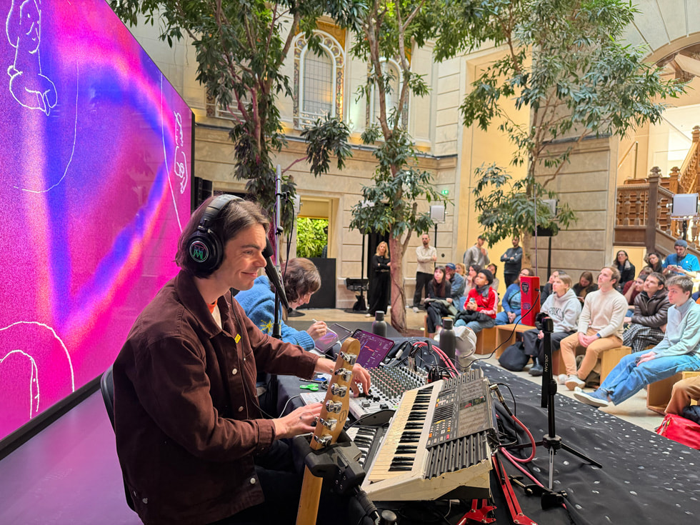 巴黎 Apple Champs-Élysées 零售店内，Pi Ja Ma 坐在 SOPORI FM 旁边，在 iPad 上作画，身后是显示插画作品的大屏幕。