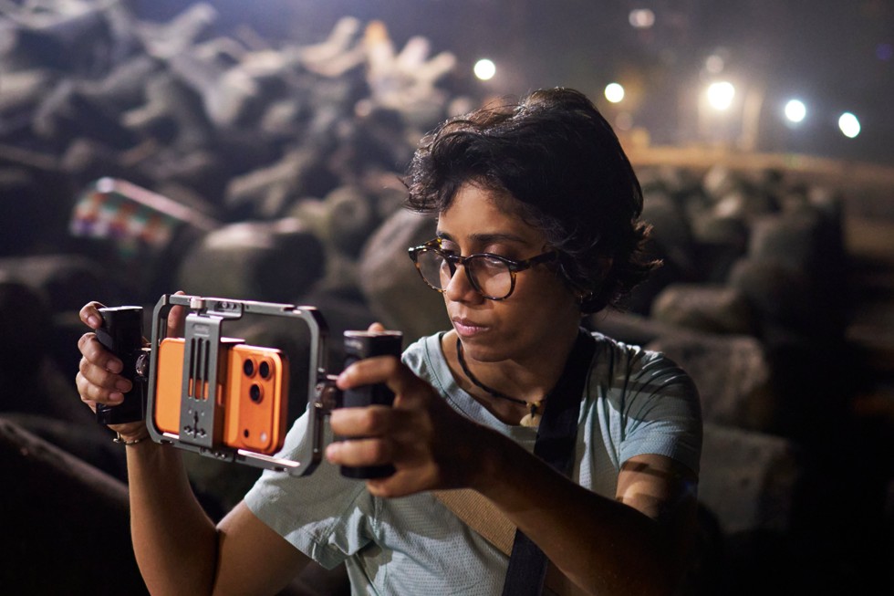 Shreela Agarwal 举着装有摄影支架的 iPhone 17 Pro Max，进行户外夜景拍摄。