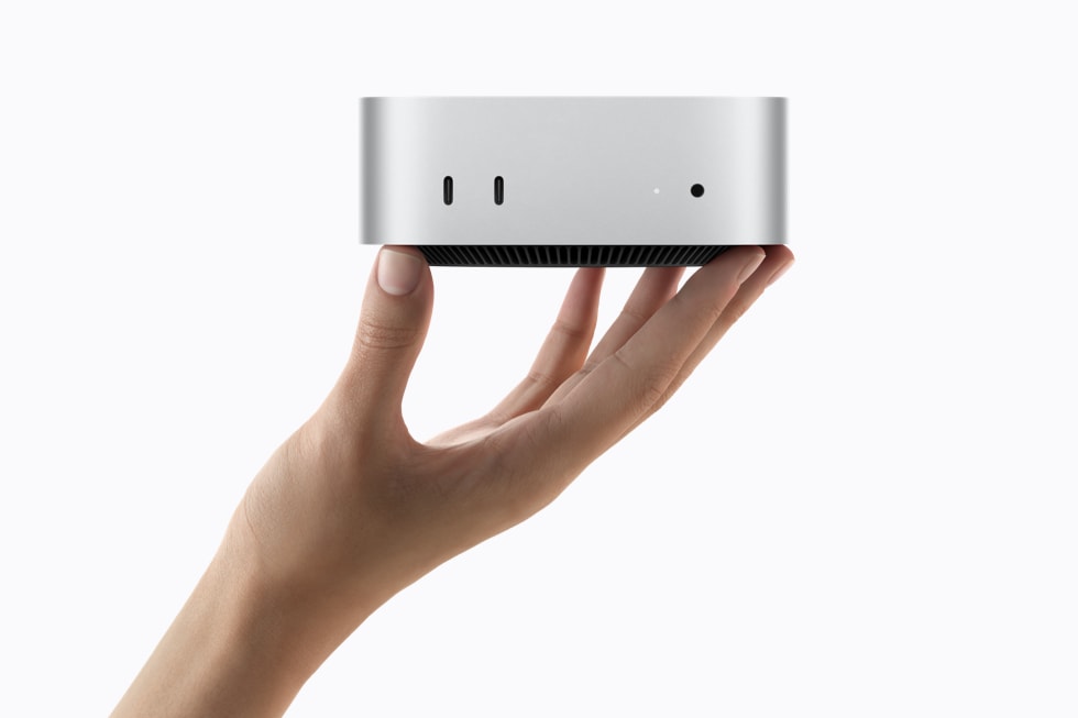 一个人手持银色 Mac mini，展示设备正面的各个端口。