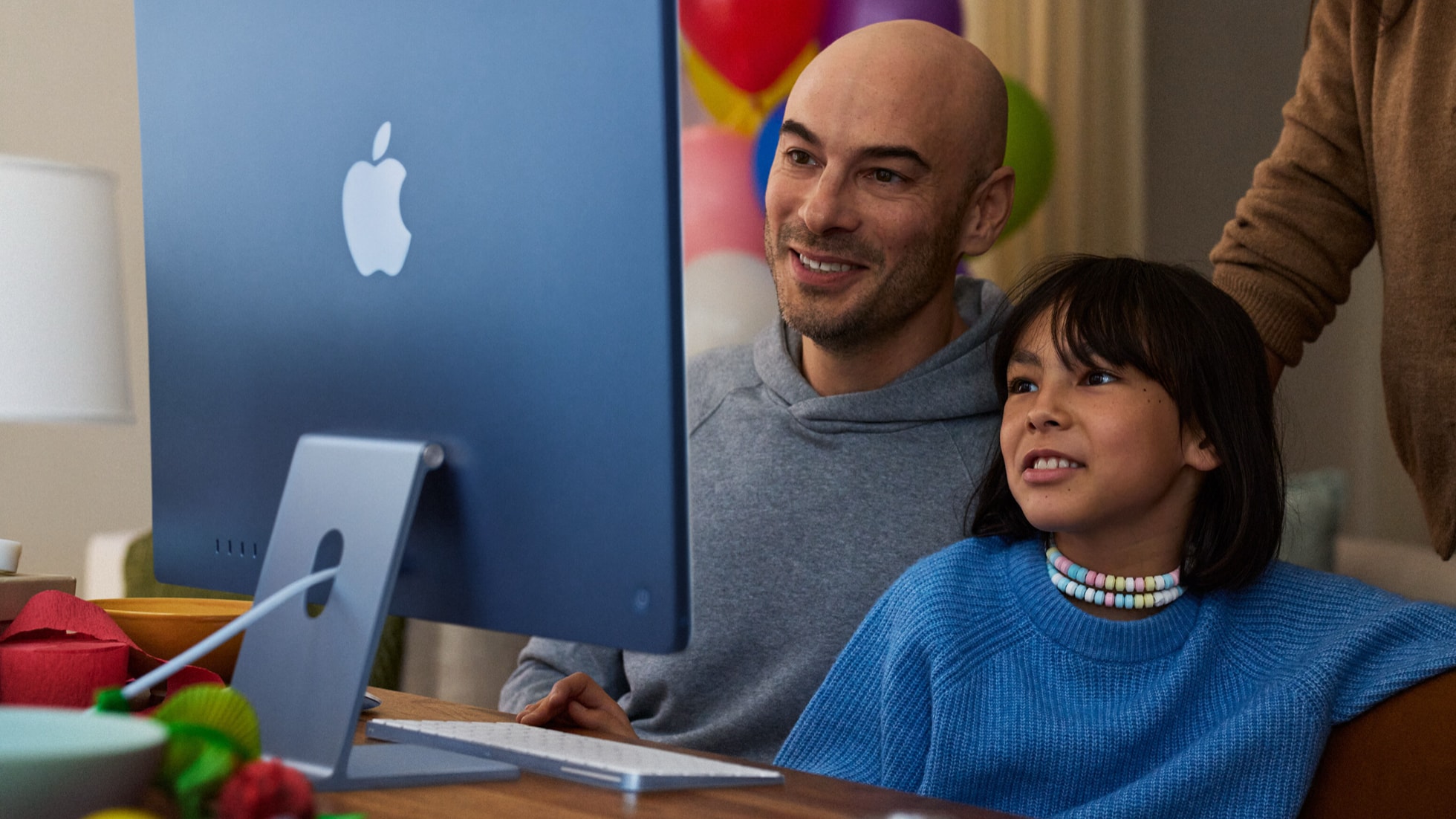 一个小孩在成人的监督下使用 iMac。