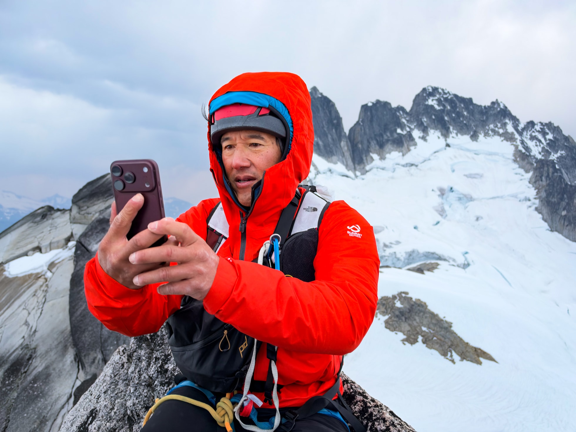 摄影师 Jimmy Chin 身穿登山装备，手持 iPhone 18 Pro 站在山顶。