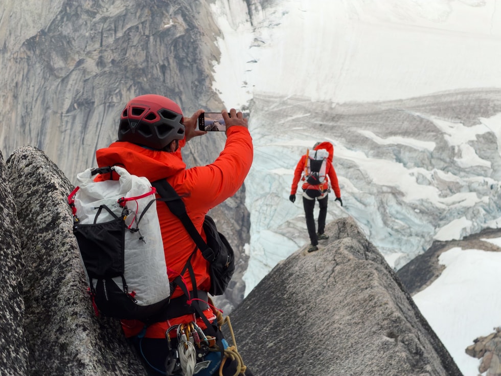 摄影师 Jimmy Chin 身穿登山装备，手持 iPhone 18 Pro 为一名登山者拍照。
