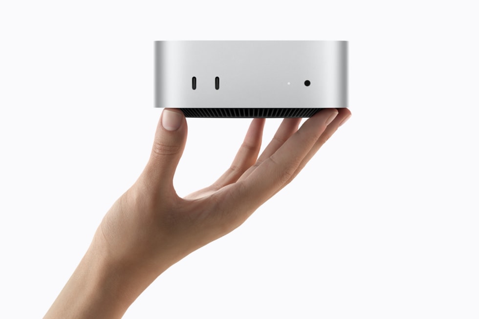 一只手举着 Mac mini，背景为白色。