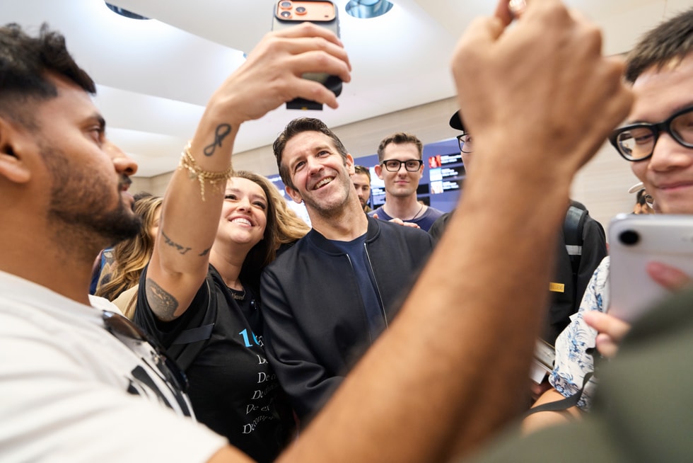 Apple 第五大道零售店内，John Ternus 面带笑容，与一位顾客合影。