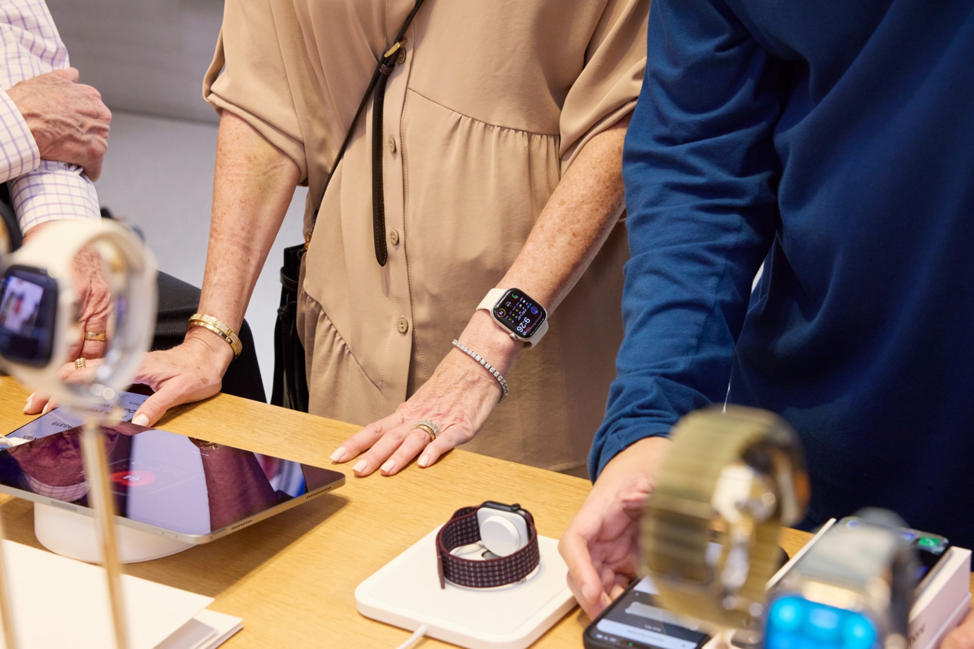 Apple 第五大道零售店的 Apple Watch 展示桌前，顾客在试戴与 iPad 和 iPhone 配对的 Apple Watch 表款。
