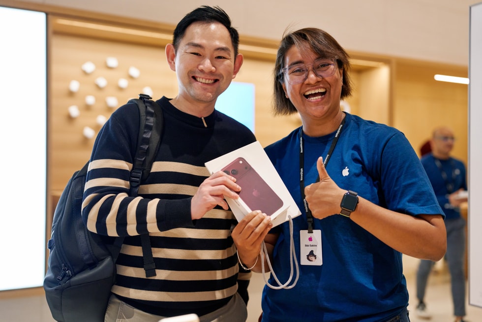 一位顾客和一名团队成员在 Apple The Exchange TRX 零售店内面带微笑，手里举着 iPhone 18 Pro。