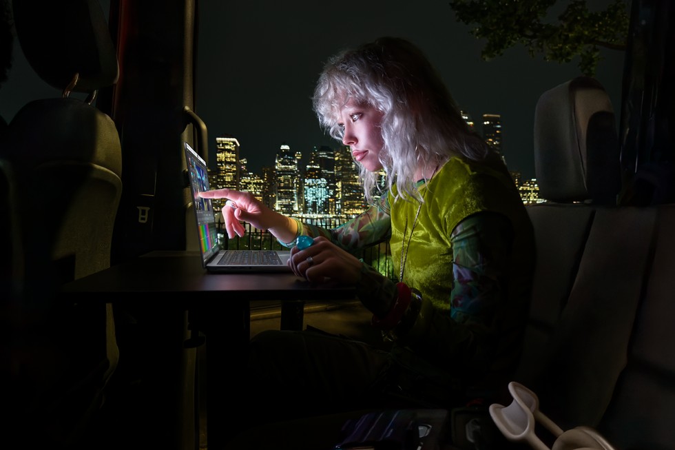 一位用户在较暗的环境中使用配备 PROLED XDR 显示屏的 MacBook Pro，身后是明亮的城市景观。