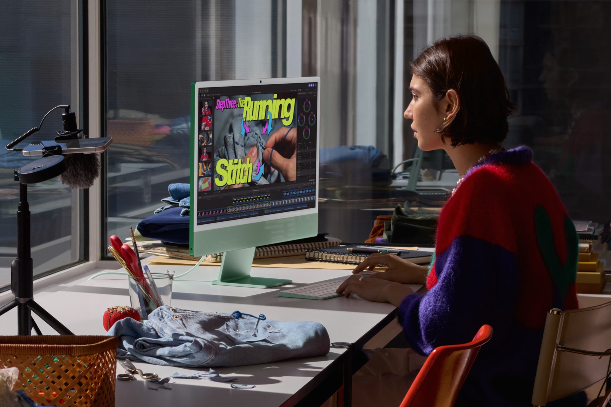 一位用户坐在搭载 M6 芯片的绿色 iMac 前剪辑视频，旁边是一件缝纫作品。