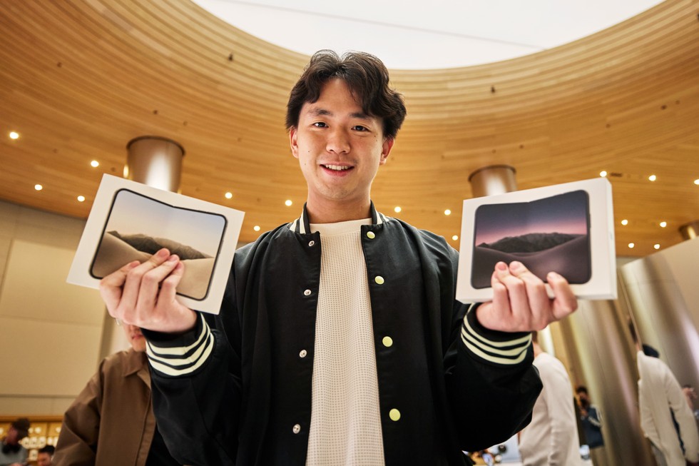 Apple 静安零售店内，一位顾客拿着两台未拆封的 iPhone Duo 设备露出笑容。