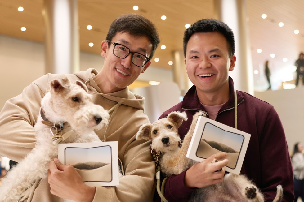 Apple 静安零售店内，两名顾客抱着新购入的 iPhone Duo 和宠物狗。