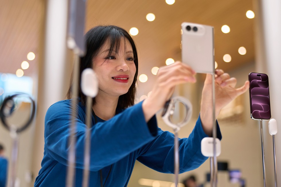 Apple 静安零售店内，一名 Apple 团队成员正在展示桌边调整一台星光白色 iPhone Duo 设备的位置。