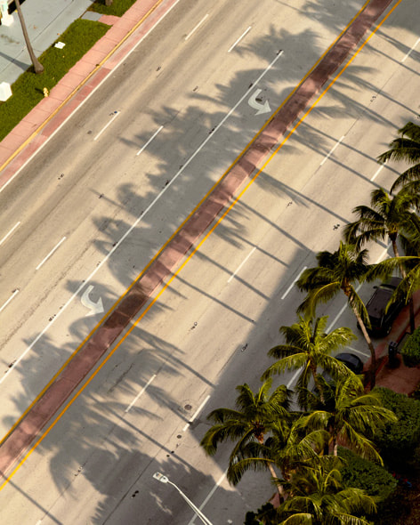 在摄影师在酒店阳台上用 iPhone 16 Pro 拍摄的照片中，棕榈树在迈阿密一条空荡荡的大街两旁投下阴影。