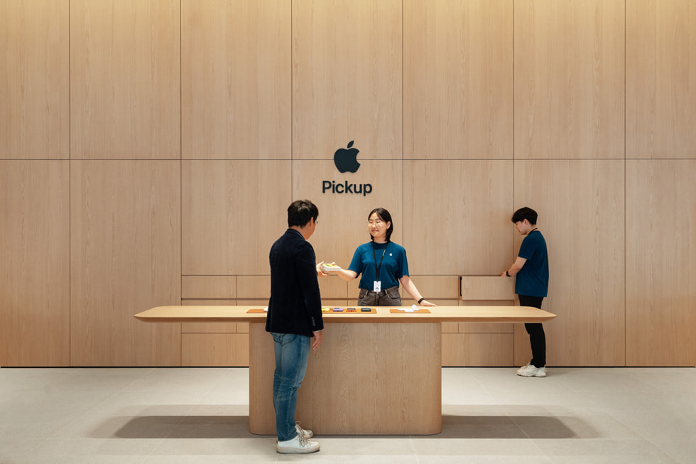 Apple Gangnam 零售店内的 Apple Pickup 到店取货服务区、展示桌和嵌木饰墙面。