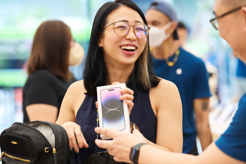 Apple Orchard Road 零售店内，一位顾客正在从团队成员手中接过购买的 iPhone 14 Pro。