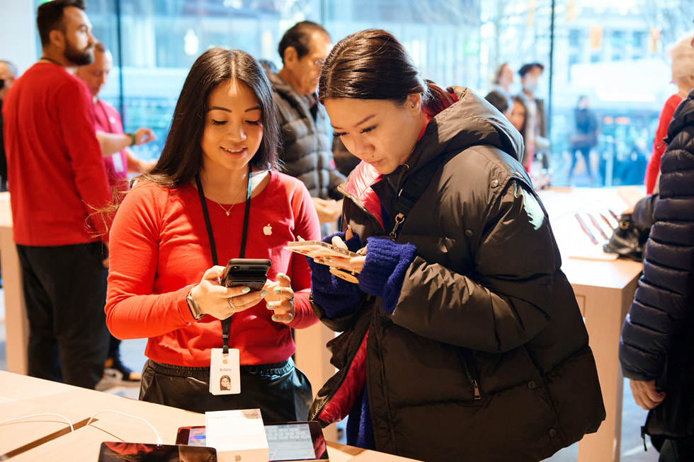 加拿大温哥华全新 Apple Pacific Centre 零售店内，顾客正在展示新购买的产品。