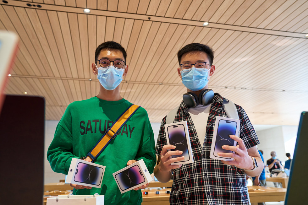 Apple 三里屯零售店内，两位顾客各自手持 iPhone 14 Pro 设备。