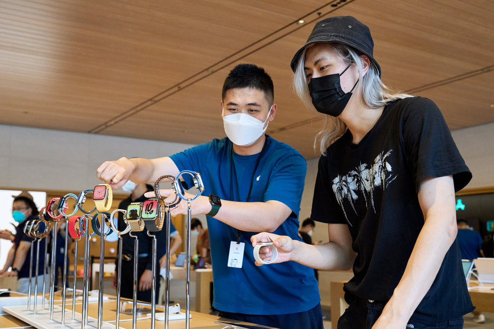 Apple 三里屯零售店内，一名团队成员正在向顾客展示 Apple Watch 设备。