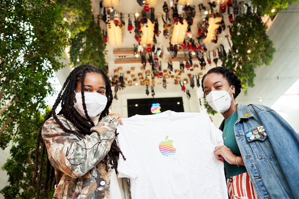 两位顾客在 Apple The Grove 手持一件 Apple 品牌图案的 T 恤。