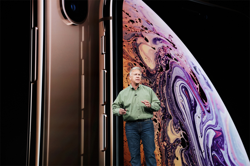 Phil Schiller in front of iPhone Xs screen on stage.