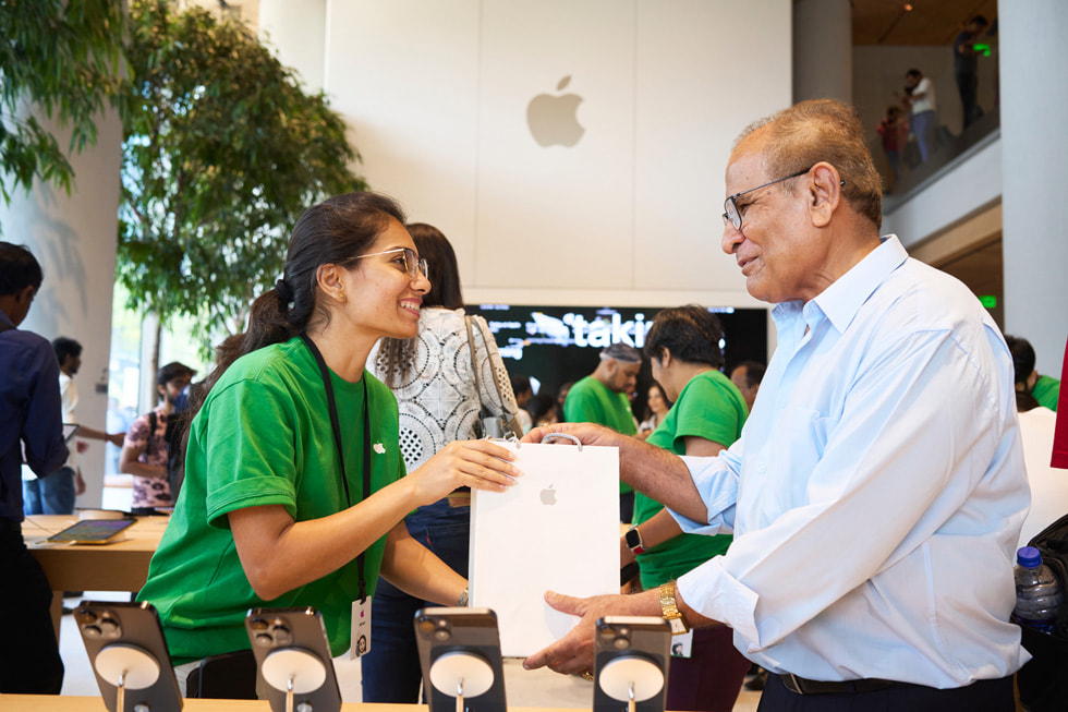 一位 Apple BKC 零售店团队成员向顾客呈现他购买的产品， 