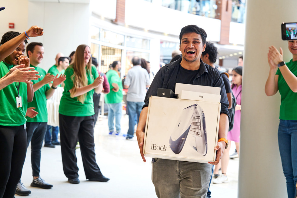 一位面带微笑的顾客为团队成员展示他的古董级 Apple 产品。