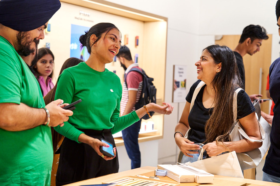 一位面带微笑的顾客正在与两名 Apple 团队成员交谈。