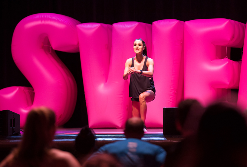 Kayla Itsines 在台上的字母型气球前示范训练环节。