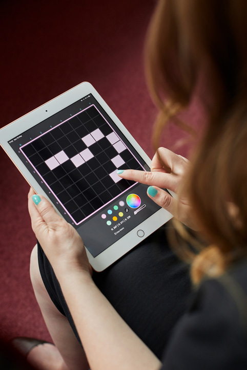 一名女性使用 imagiLabs app 的特写。她正在黑色背景上用粉色方块设计图案。